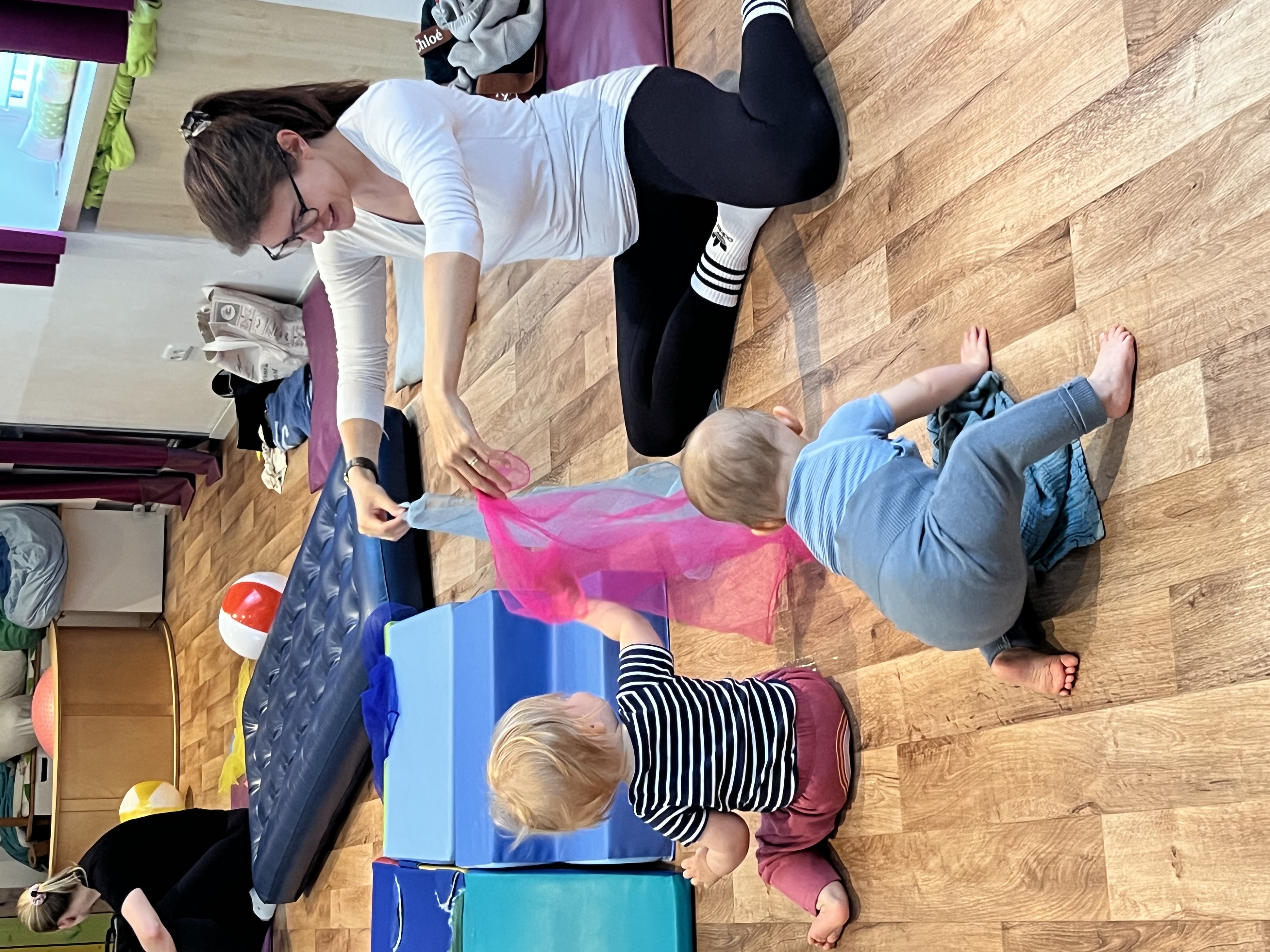 Zwei Babys und Mutter spielen mit Tuch